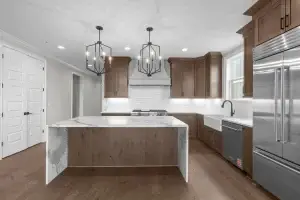Custom transitional kitchen featuring stained wood shaker style cabinets, a white farmhouse sink, and a marble waterfall island.