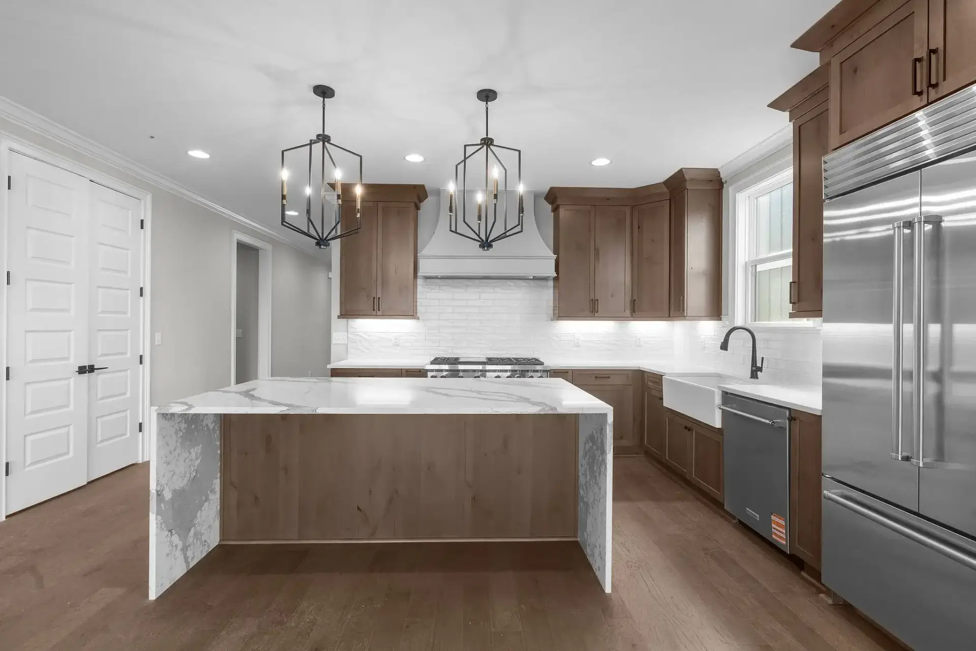Custom transitional kitchen featuring stained wood shaker style cabinets, a white farmhouse sink, and a marble waterfall island.