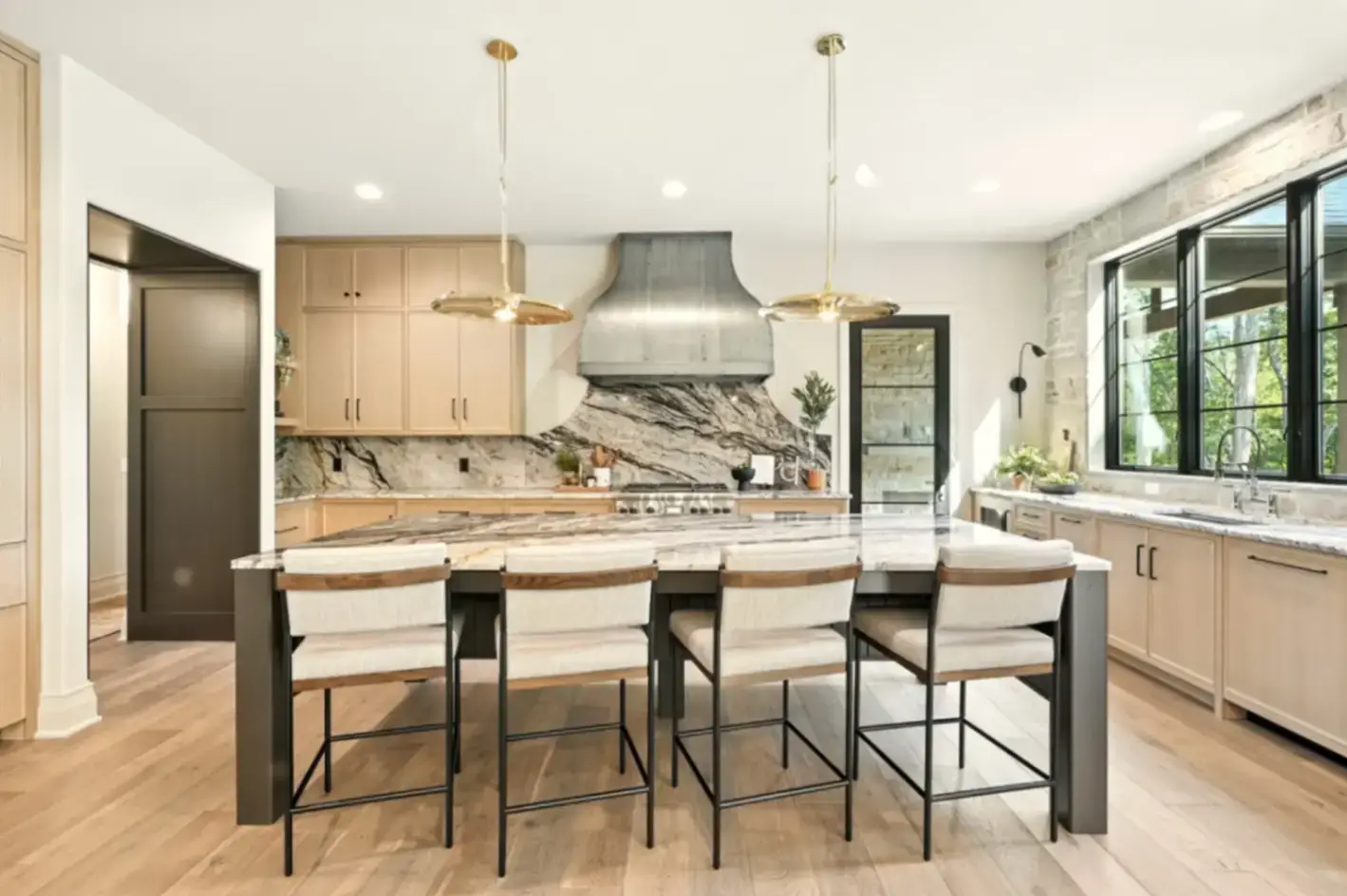 Centered view of an organic modern kitchen highlighting rift sawn white oak slim shaker cabinets, a custom zinc range hood, and a dramatic bookmatched quartzite waterfall island.