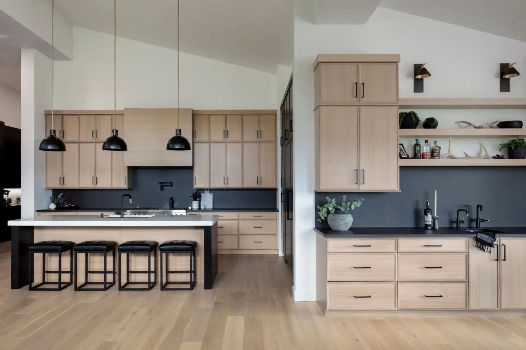 Wide angle kitchen view highlighting a custom oak vent hood, integrated cooking lines, a center island, and an adjacent secondary wet bar counter.