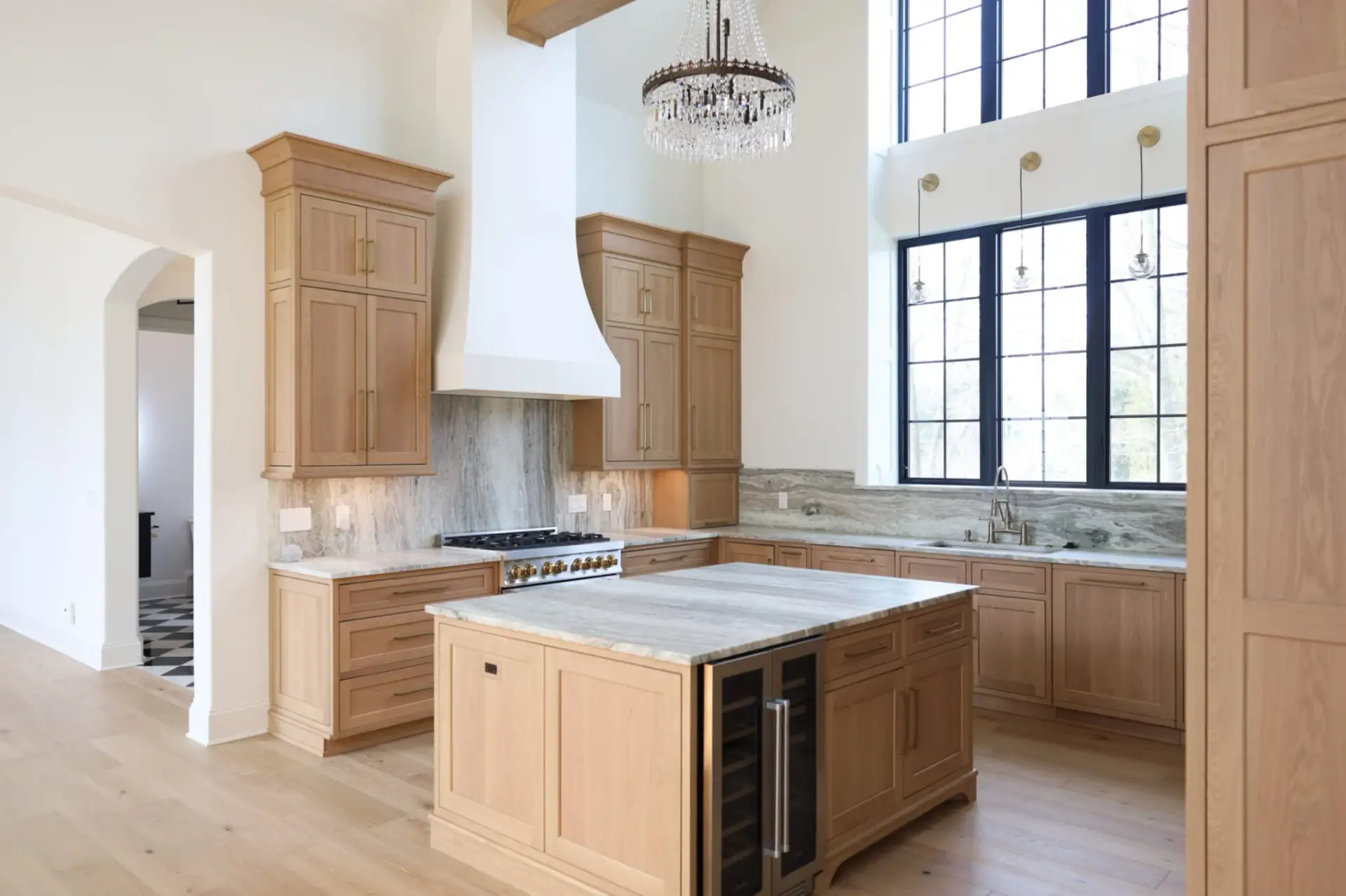 Close-up view of an oversized white plaster range hood flanked by custom rift-sawn white oak upper and base cabinets with integrated refrigeration.