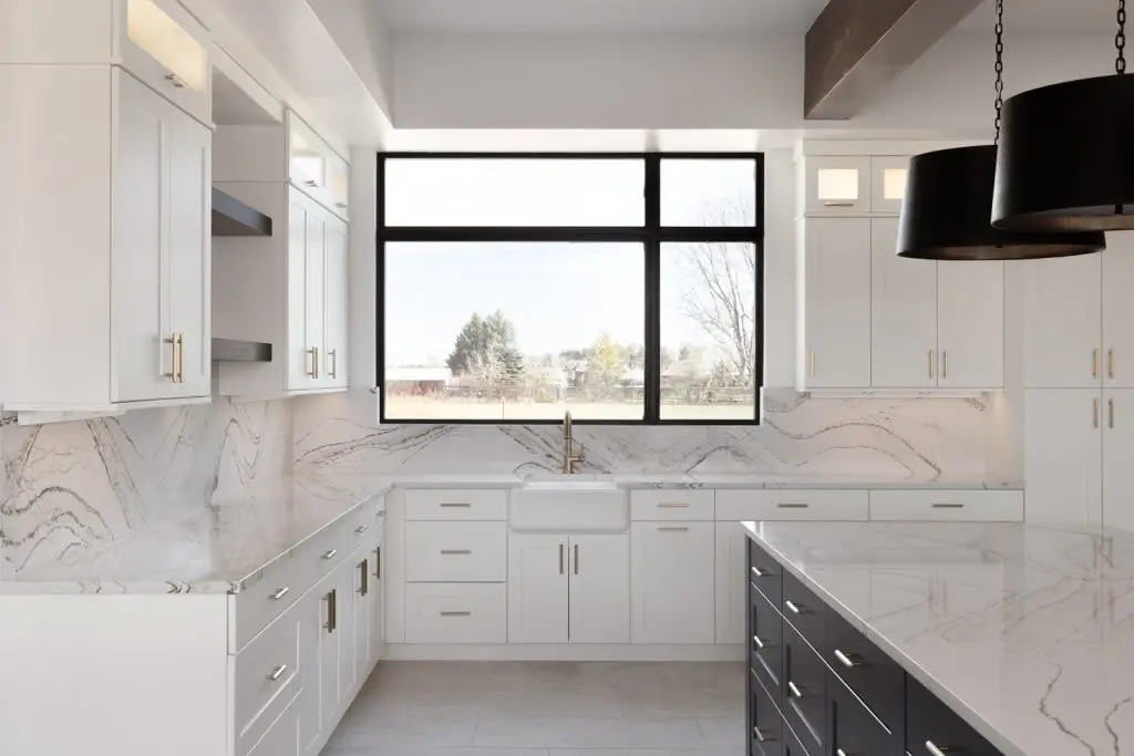 Detailed view of white lacquered shaker cabinets with a white farmhouse sink and gold faucet in a luxury home.