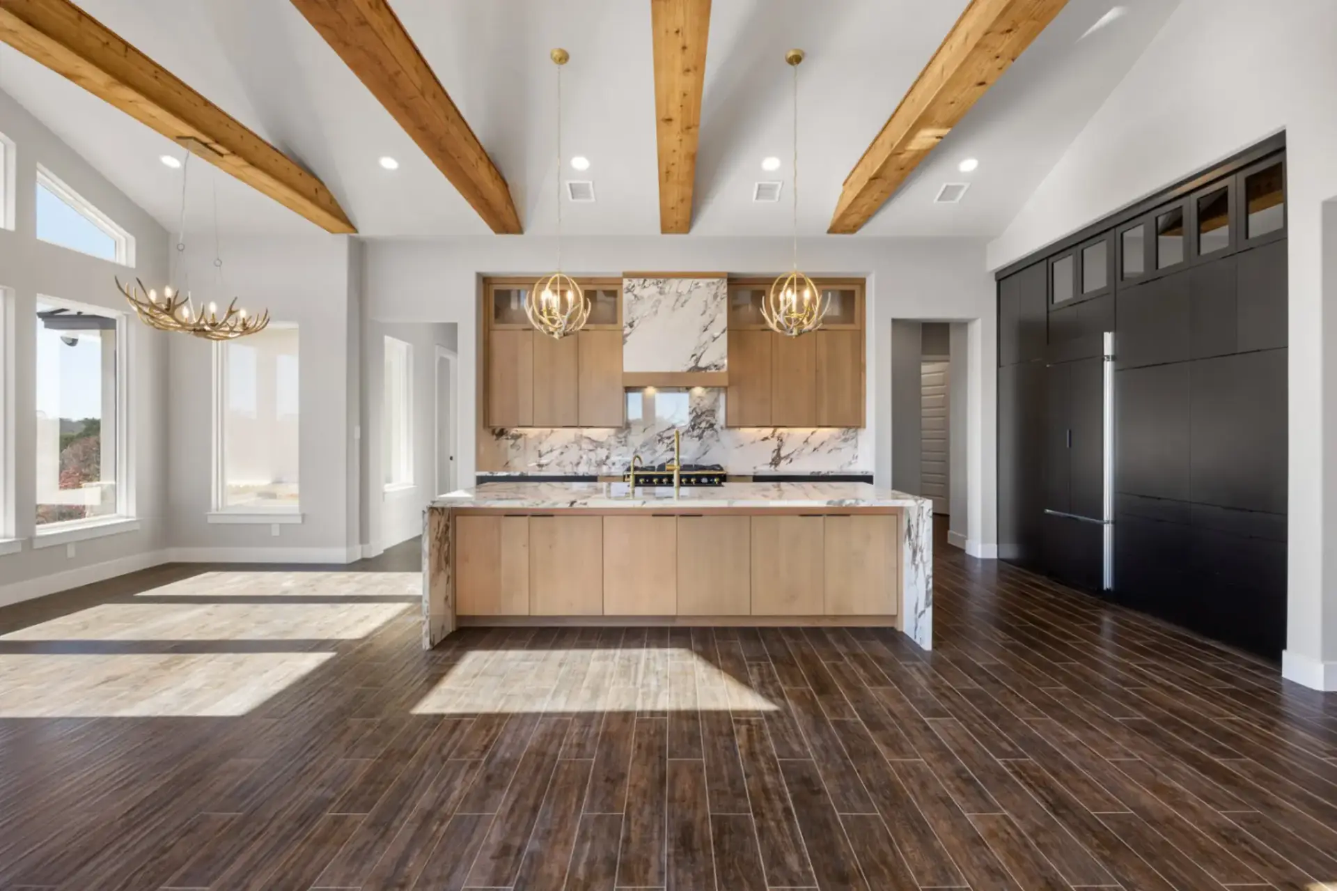 Two-tone modern mountain kitchen highlighting an open layout with matte black kitchen cabinets and a natural marble waterfall kitchen countertop.
