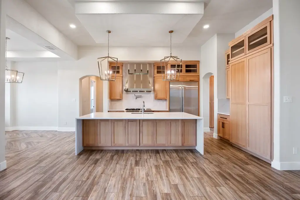 Broad open view of a luxury contemporary kitchen designs layout with a large waterfall kitchen island, natural wood shaker cabinets, and professional ranges.
