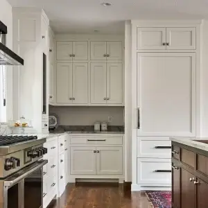 Luxury custom kitchen design featuring off white shaker kitchen cabinets with a flush inset face-frame structure. Includes a built-in integrated refrigerator panel, dark marble countertops, a professional stainless steel range stove, and polished chrome handles, contrasting with a dark stained wood island.