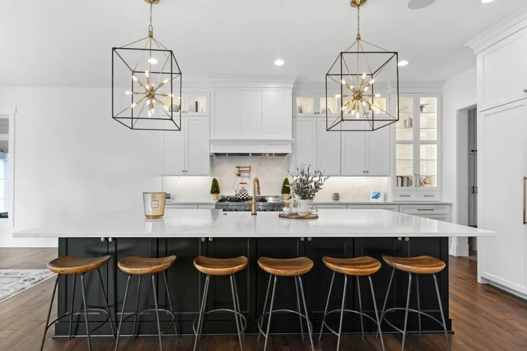 Symmetrical front perspective of two tone black and white kitchen cabinets featuring a dark base island with barstools.