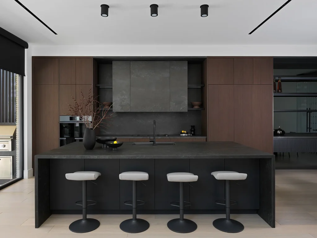 Symmetrical front perspective showcasing a monolithic kitchen island black structure featuring a waterfall stone countertop edge and four barstools.