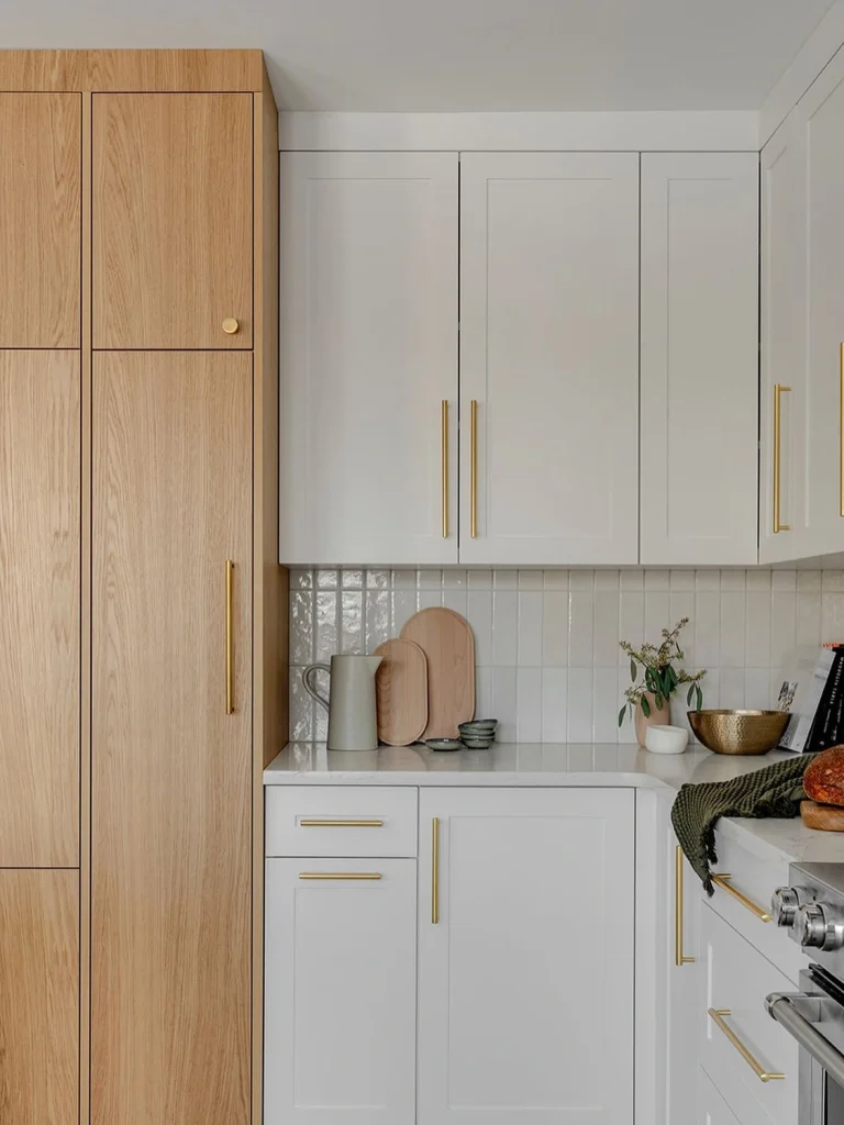 Architectural interior of a modern two-tone G-shaped kitchen with natural white oak flat panel base cabinets, crisp white slim shaker uppers, and seamless quartz counter.
