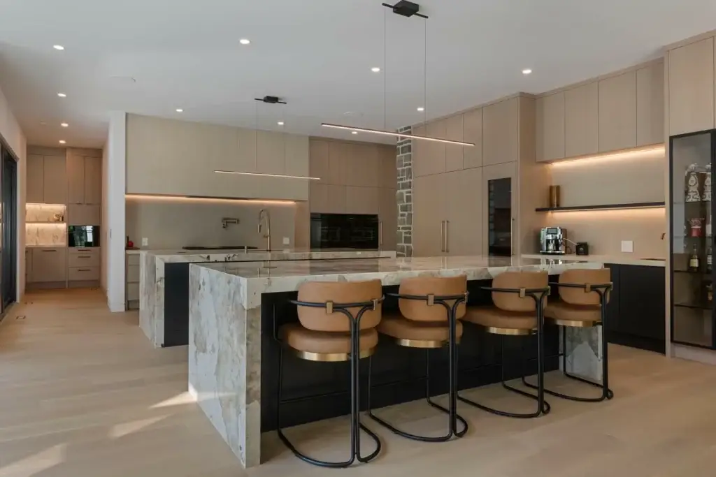 Wide spatial view of an oak cabinet veneer kitchen featuring dual quartzite waterfall islands and leather barstools.
