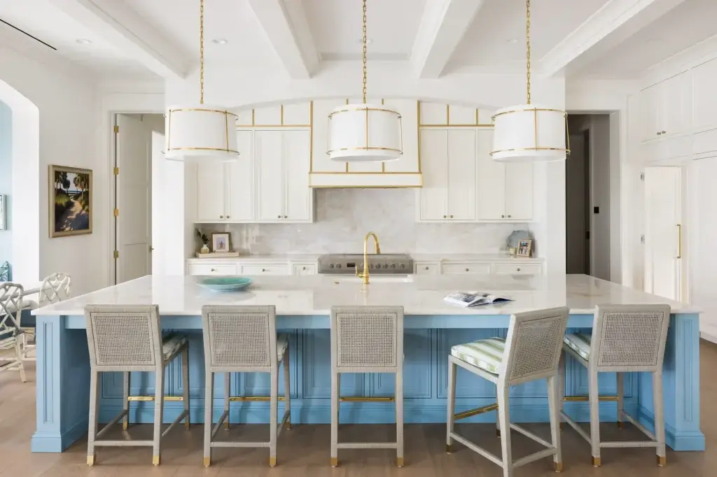 Direct perspective of two tone kitchen cabinets blue island featuring brass-trimmed white shade pendants and cane barstools.