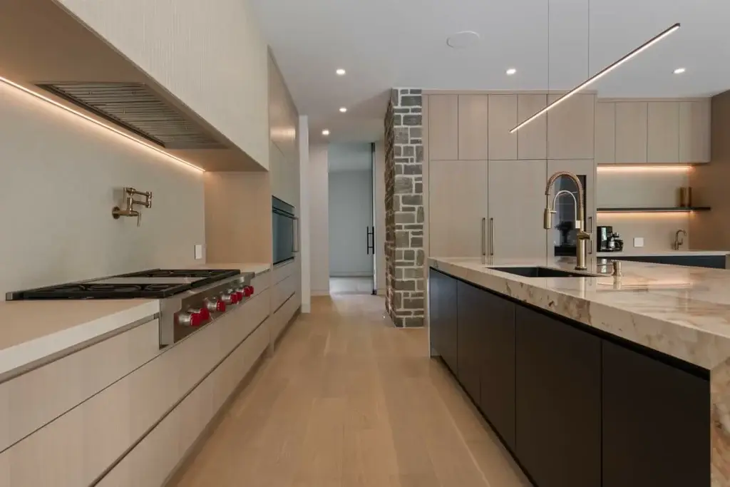 Close perspective of white oak slab kitchen cabinets wall running parallel to a dark matte prep island with a brass gooseneck faucet.