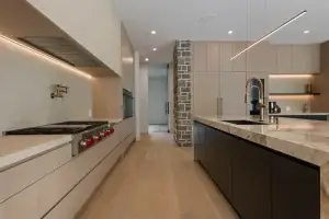 Close perspective of white oak slab kitchen cabinets wall running parallel to a dark matte prep island with a brass gooseneck faucet.