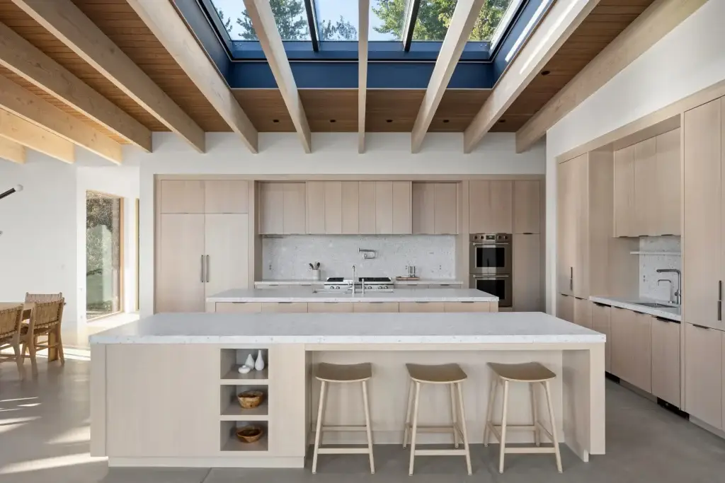 Wide architectural perspective displaying whitewash oak kitchen cabinets beneath an expansive glass skylight ceiling system.