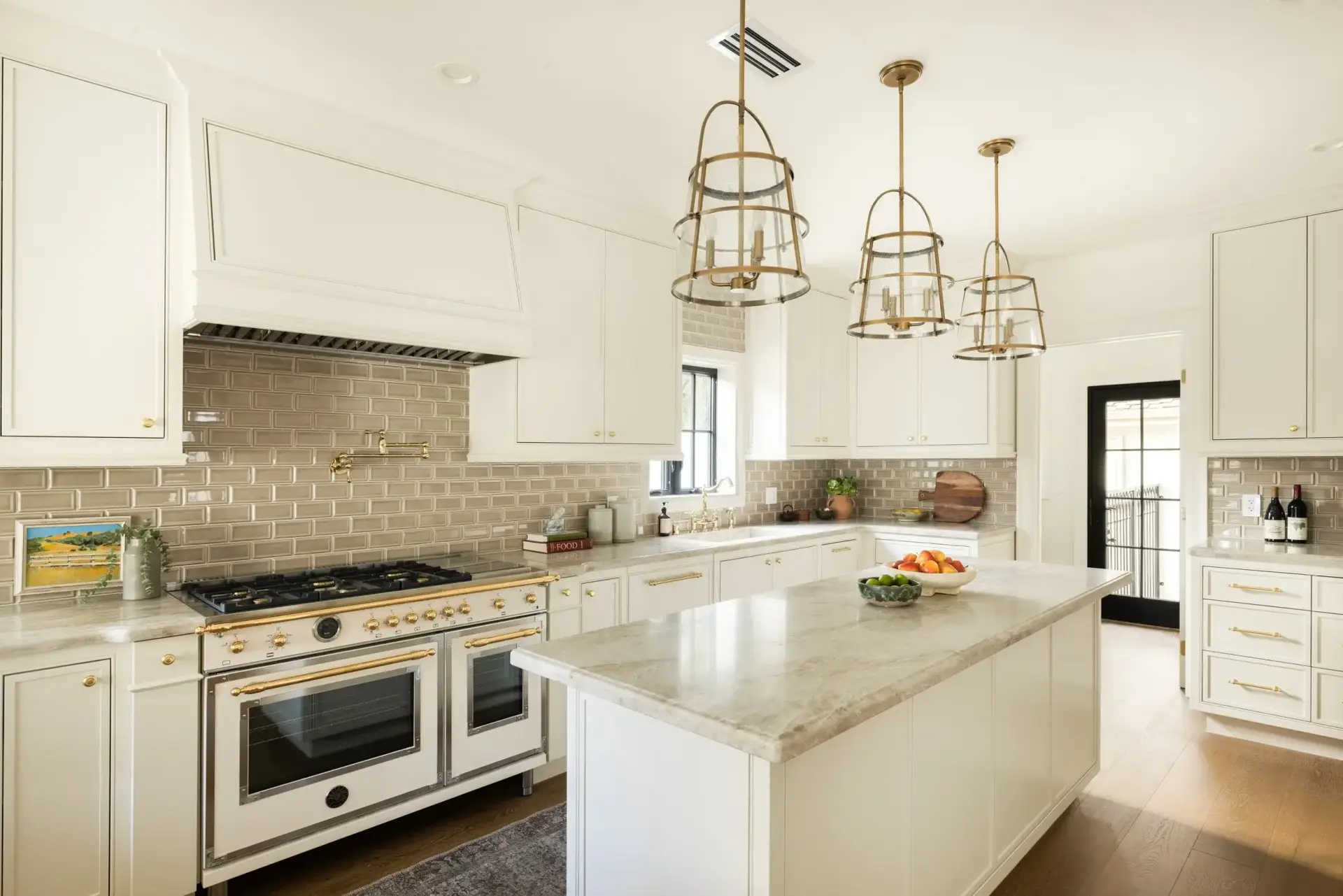 Wide perspective of a cream cabinets kitchen featuring a large quartzite prep island, vintage white range, and brass pendant lights.