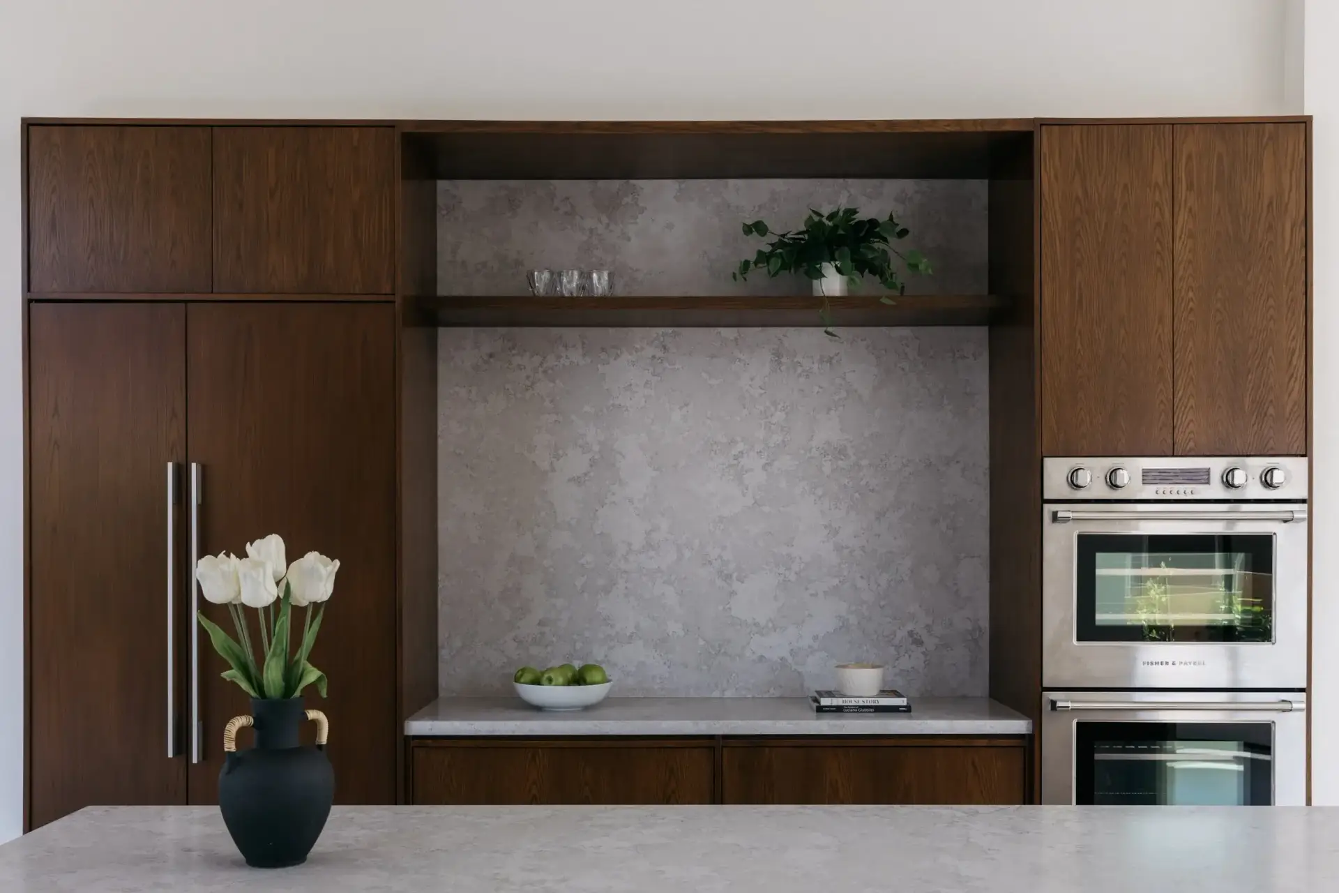 Front view of a dark oak cabinet wall integrating a panel-ready refrigerator, double ovens, and coffee alcove.