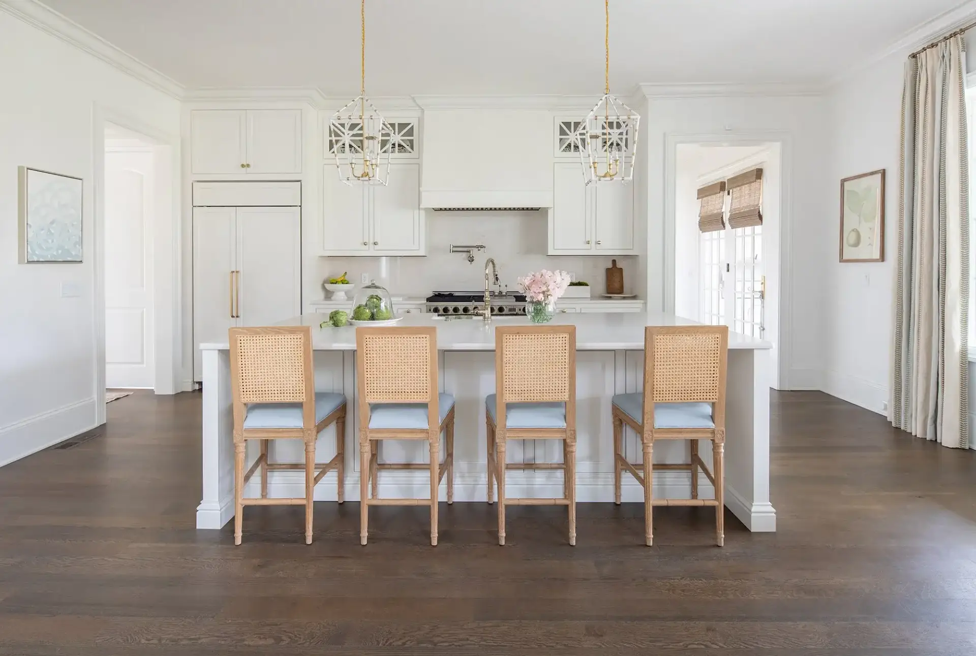 Symmetrical center view of a french country kitchen showcasing a large white island with cane back counter stools and lantern lights.