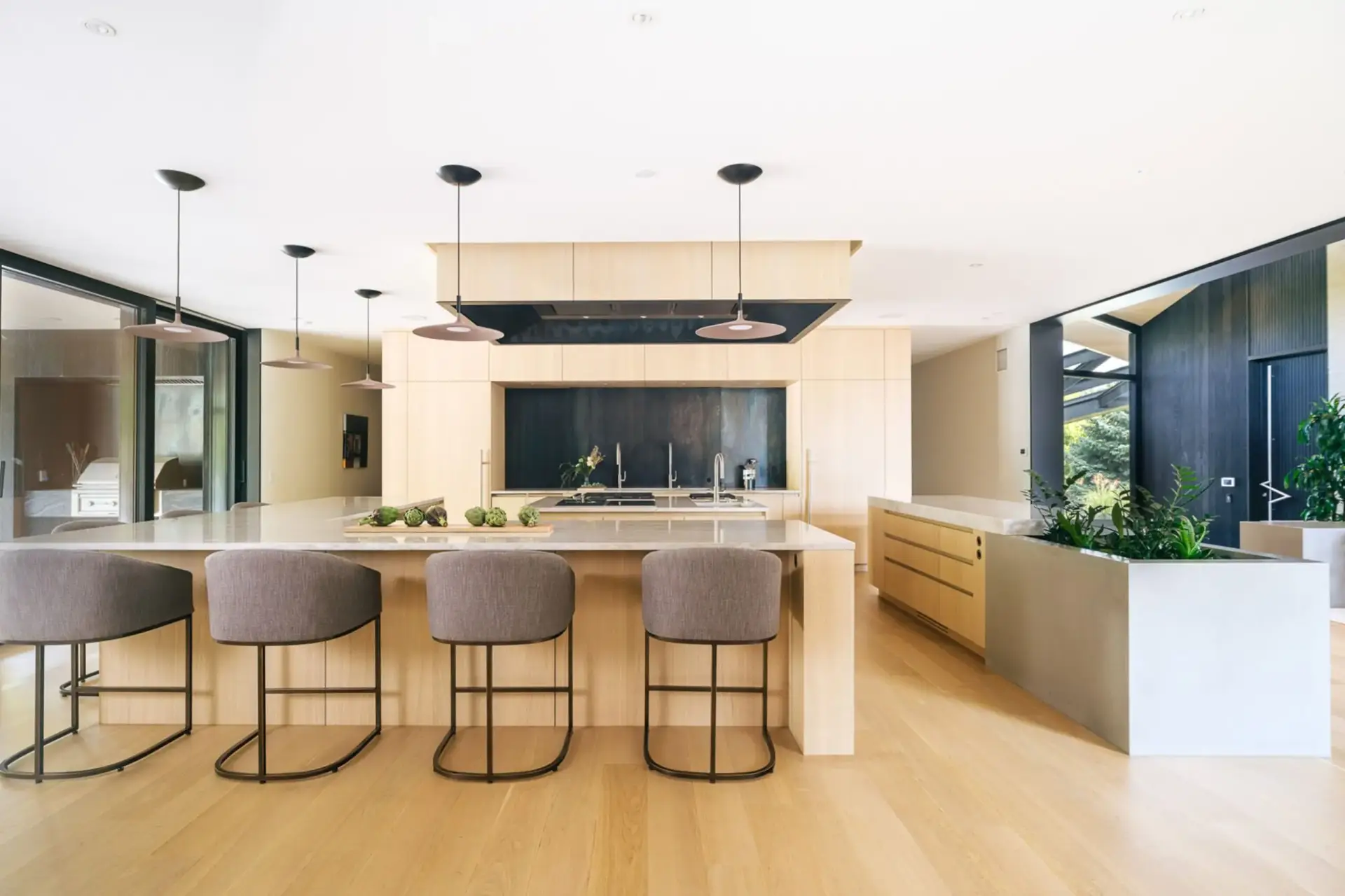 Symmetrical center view of modern slab door kitchen cabinets showcasing the preparation island, barstools, and black accent wall.