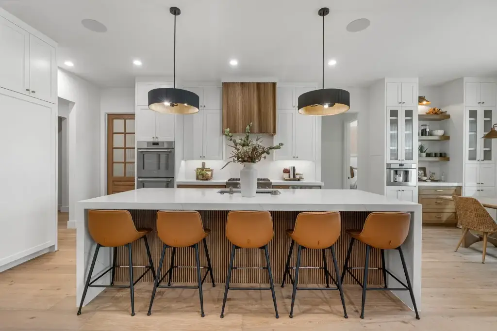 Center view of a modern transitional kitchen with a slatted oak island, quartz waterfall counters, and black pendant lights.