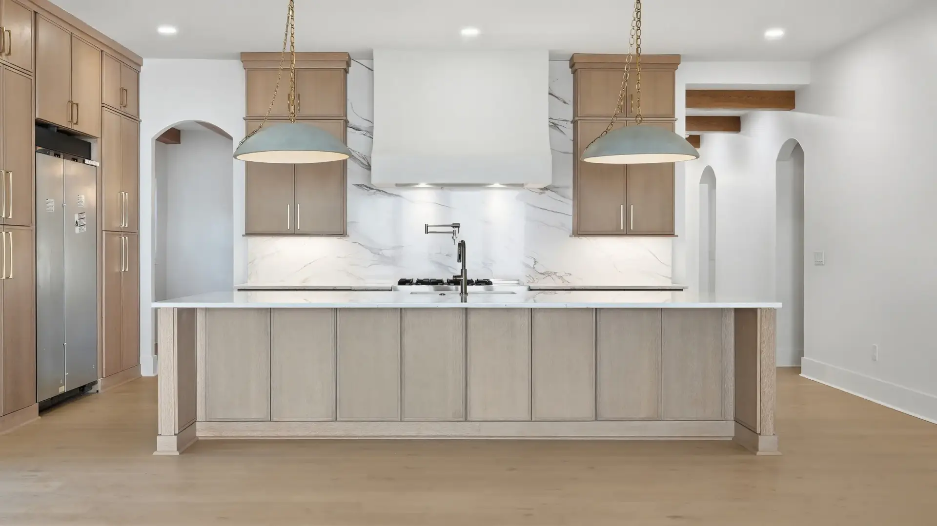 Symmetrical center view of slim shaker white oak cabinets featuring a large prep island, plaster hood, and dome pendants.