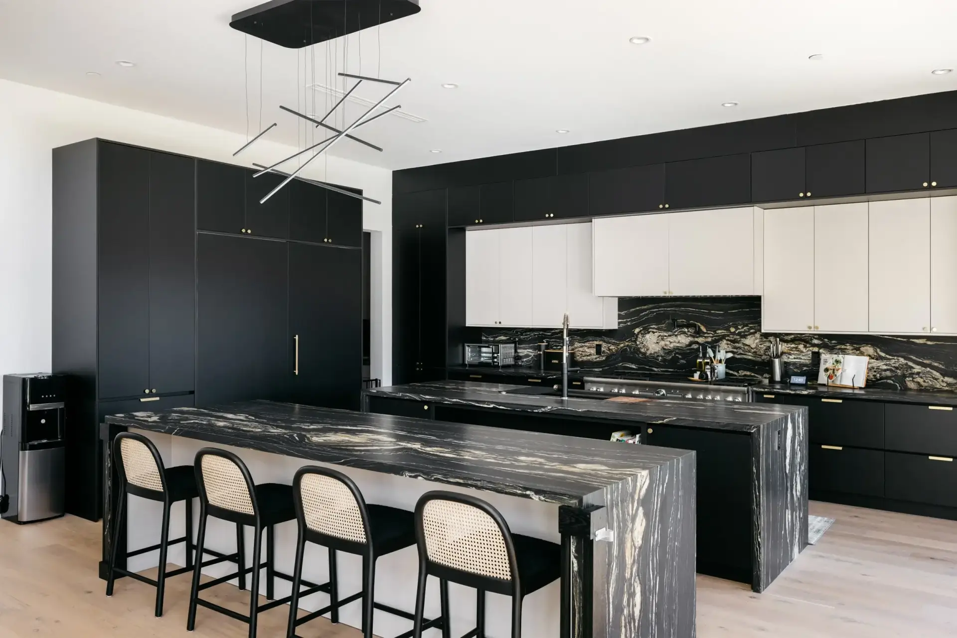 Wide spatial angle of tall kitchen furniture with matte black tall towers and cosmic black granite islands.