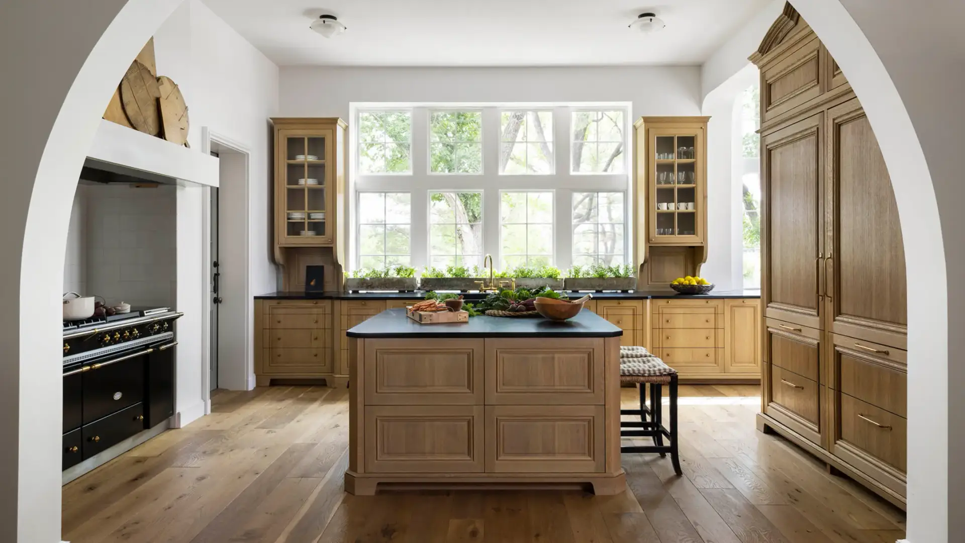 View through a white plaster archway showing a traditional english kitchen with oak inset cabinets, armoire larder, and island.