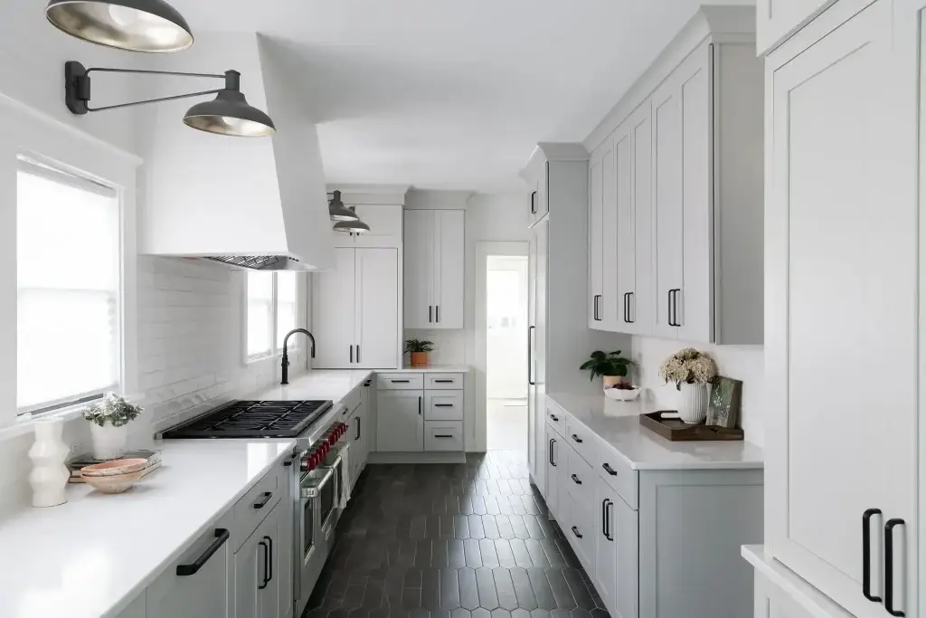 Full elevation of a white galley kitchen showcasing parallel work counters, white range hood, and black hex flooring.