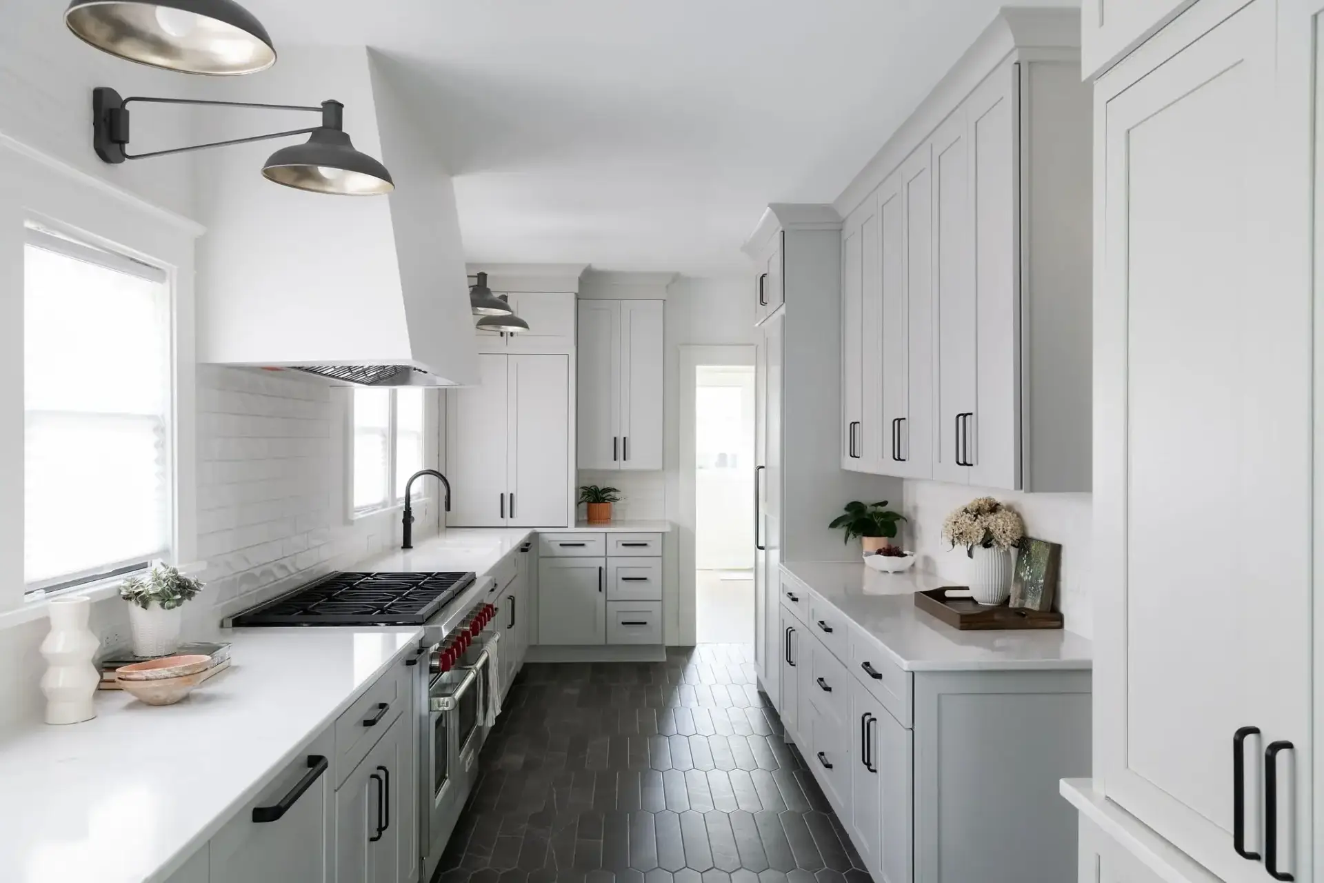 Full elevation of a white galley kitchen showcasing parallel work counters, white range hood, and black hex flooring.