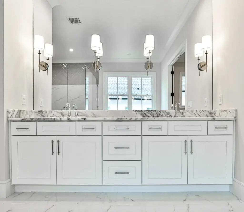 Bathroom vanity with double sink featuring white shaker doors, marble top, and wide mirror
