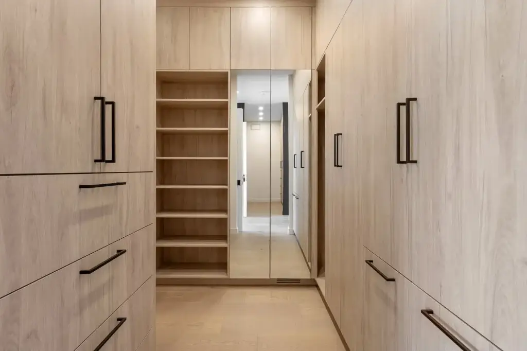 Custom built-in wardrobes and closet casework in modern light wood veneer featuring integrated drawer banks and mirror doors