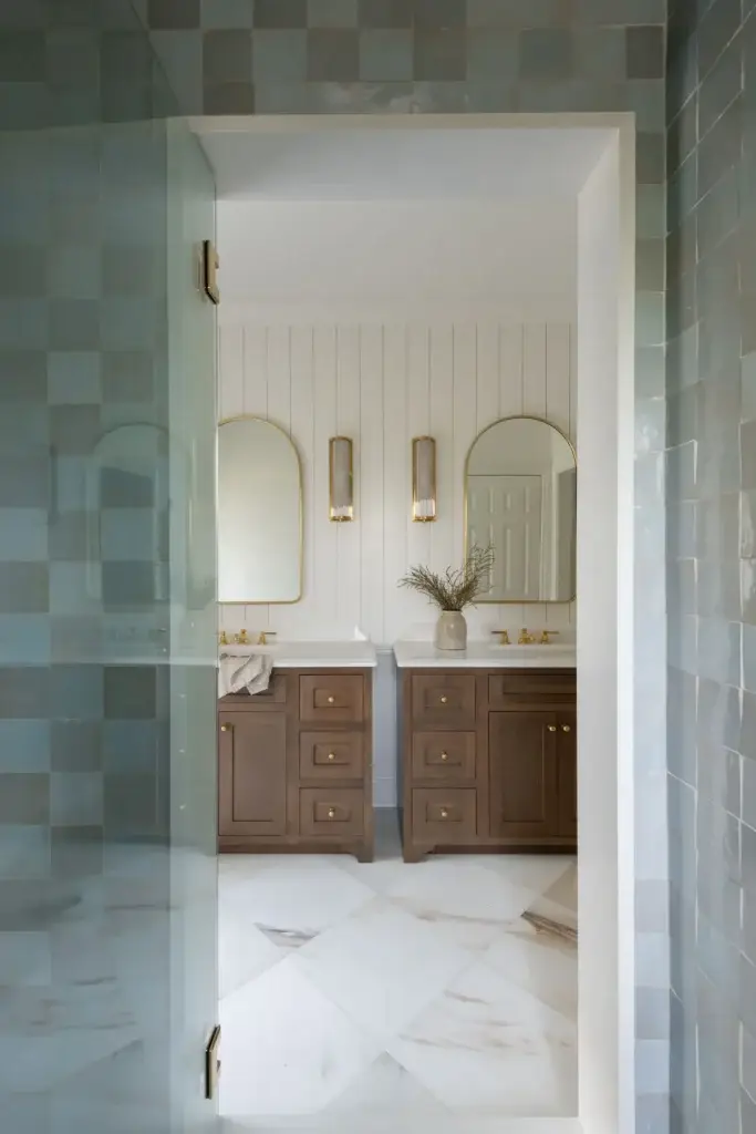 Stained bathroom vanity layout featuring oak double vanity consoles, arched brass mirrors, and white shiplap walls